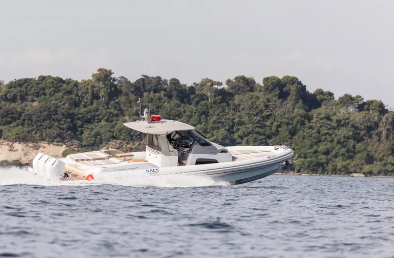  Yacht Photos Pics 2026 SACS NEW Strider 13 luxury boat cruising on open water near a forested shoreline.