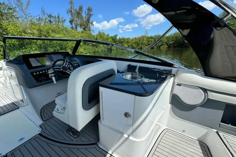  Yacht Photos Pics 2020 Cobalt R30 boat interior with helm, sink, and seating, surrounded by lush greenery.