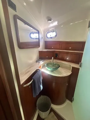 No Name Yacht Photos Pics 2019 Pursuit OS 385 Offshore bathroom with wood cabinetry, glass sink, and porthole windows.