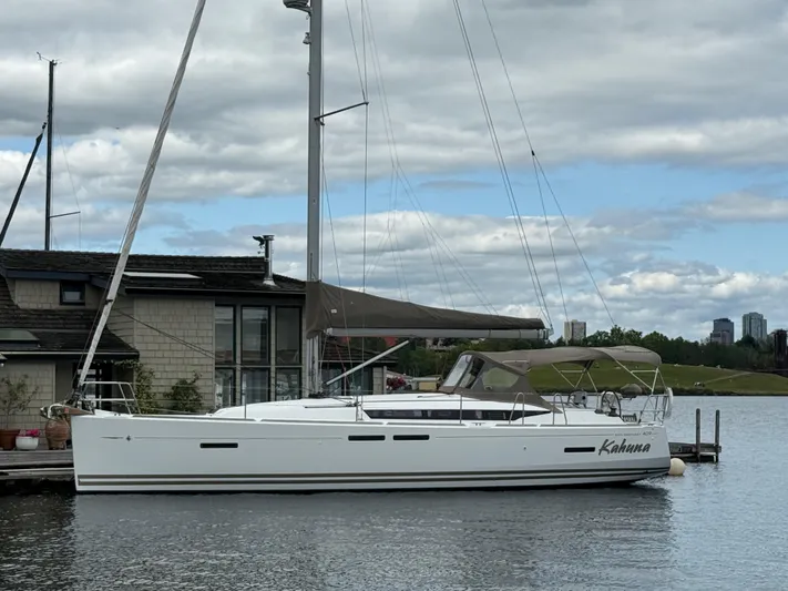 Kahuna Yacht Photos Pics Sailboat Jeanneau 409, 2011 model, docked by a waterfront house under cloudy skies.