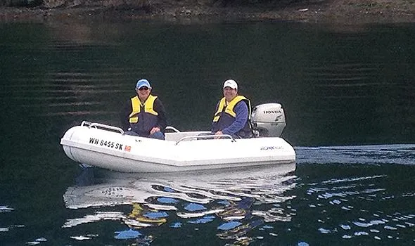 Hullabaloo Yacht Photos Pics Two people in a small boat on calm water, wearing life jackets.