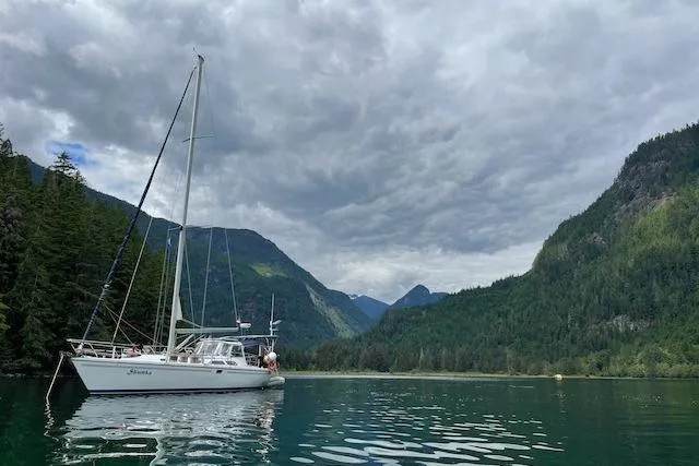 Shumka Yacht Photos Pics Catalina 42 MkII sailboat on serene lake, surrounded by lush mountains and cloudy sky.