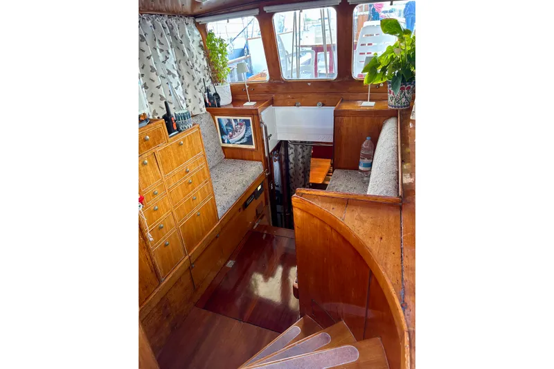Barinia Yacht Photos Pics 1950 MOLLICH Sailing boat interior with wooden cabinetry and seating, featuring plants and decor.