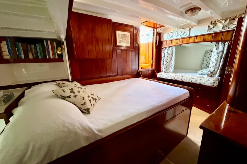 Barinia Yacht Photos Pics 1950 MOLLICH Sailing yacht cabin with wooden interior, cozy bed, and bookshelf.