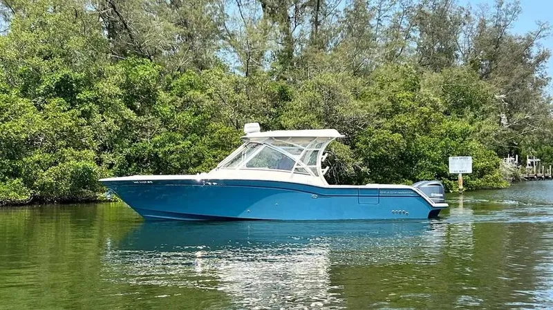  Yacht Photos Pics 2019 Grady-White Freedom 325 boat on calm water, surrounded by lush greenery.
