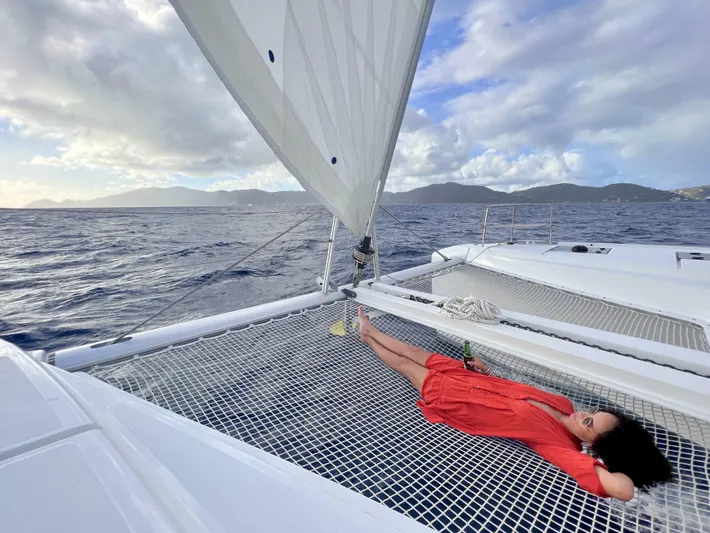 Echo Yacht Photos Pics Woman relaxing on Lagoon 50 catamaran netting, sailing with scenic ocean and mountain backdrop.