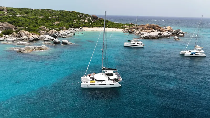 Echo Yacht Photos Pics 2023 Lagoon 50 catamaran sailing in clear turquoise waters near a rocky island.