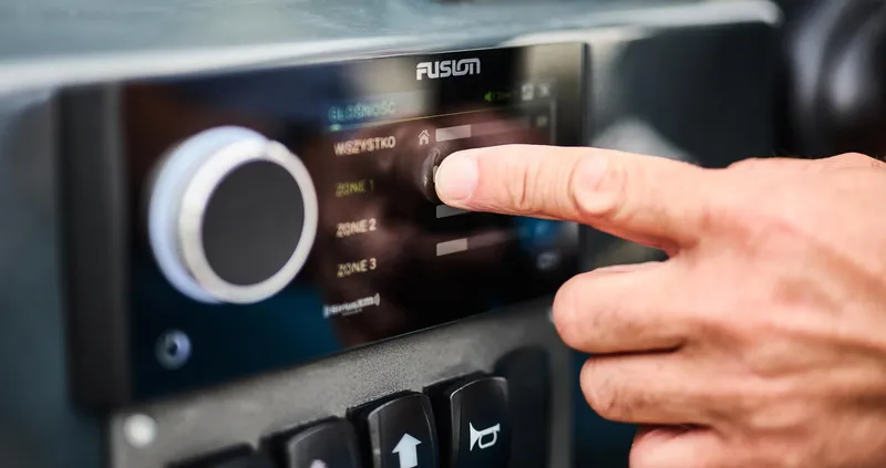  Yacht Photos Pics Close-up of a hand adjusting a Fusion audio system in a 2024 Skamander Sorrento.