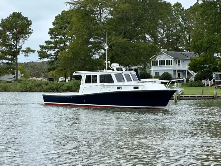  Yacht Photos Pics 2016 Custom Broad Creek 32 Downeast boat on calm water near a house and trees.