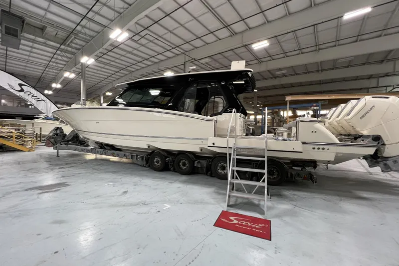  Yacht Photos Pics 2025 Scout 530 LXF boat in a showroom, featuring multiple outboard engines.