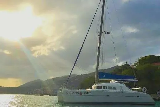 Guiding Light Yacht Photos Pics 1997 Lagoon 410 catamaran sailing at sunset near scenic coastline.