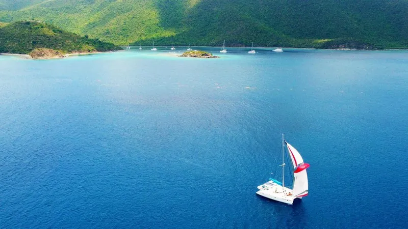 Guiding Light Yacht Photos Pics Lagoon 410 catamaran sailing in clear blue waters, lush green hills in the background.