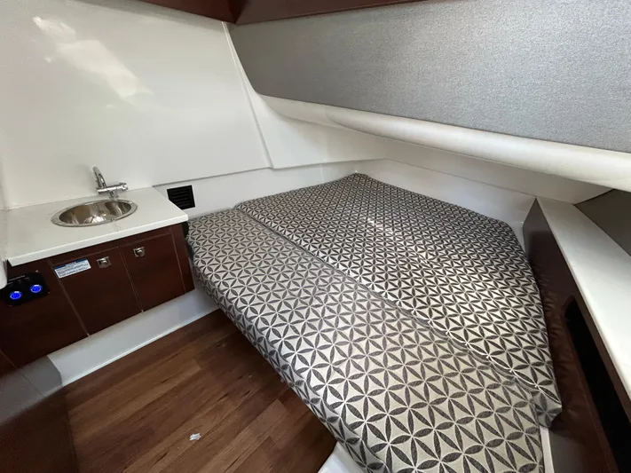  Yacht Photos Pics 2023 Chaparral 300 OSX cabin interior with bed, sink, and wooden flooring.