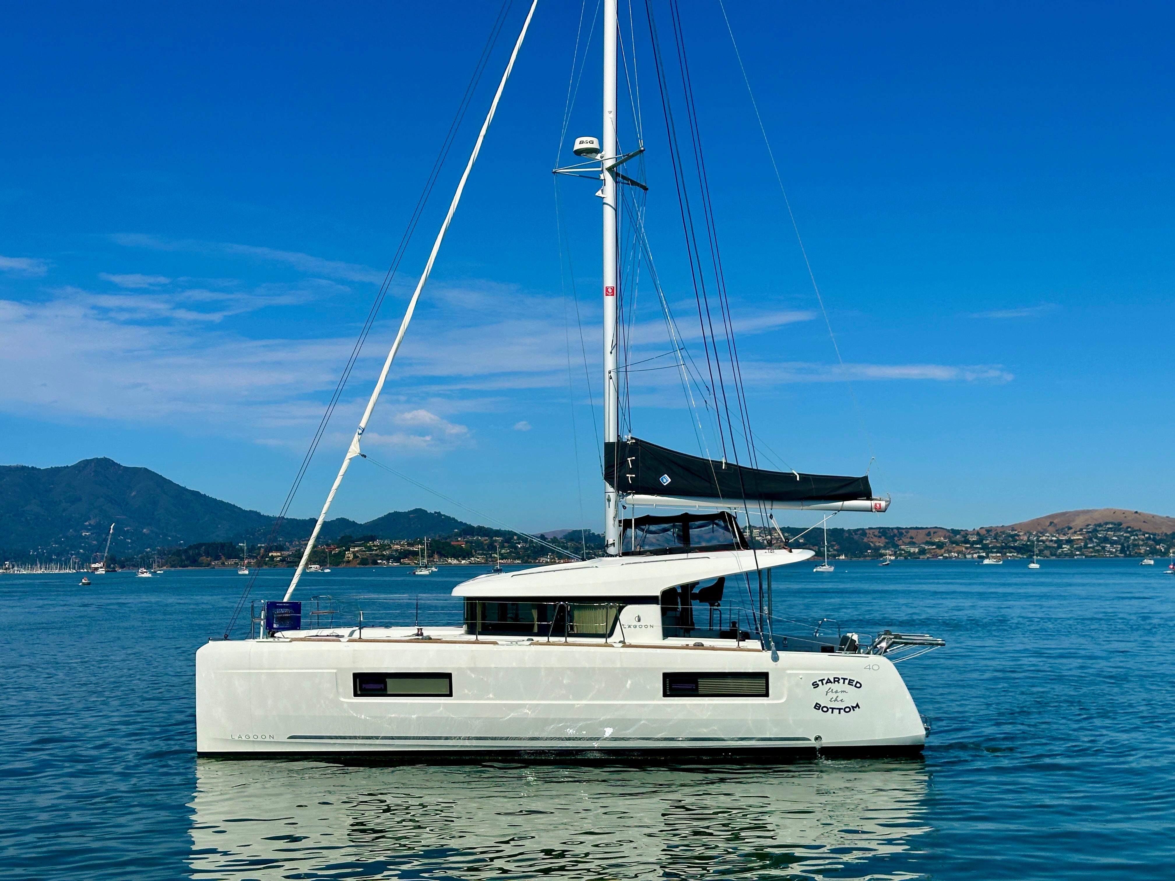 2020 Lagoon 40 catamaran sailing on calm waters with scenic mountain backdrop.