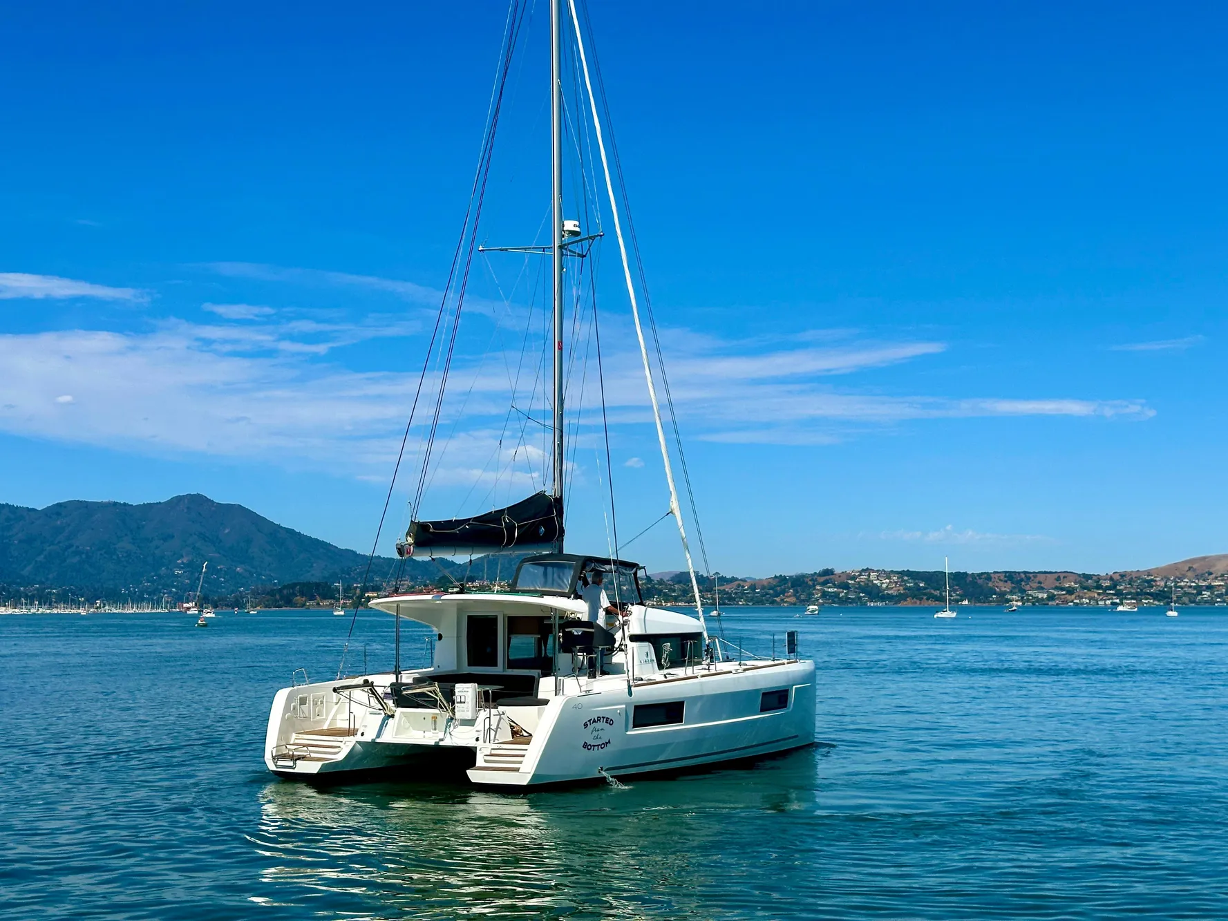 2020 Lagoon 40 catamaran sailing on a calm sea with mountainous backdrop.