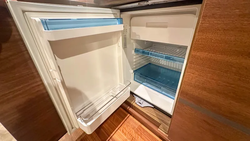 F55163 Yacht Photos Pics Open refrigerator in 2023 Princess F55 yacht, featuring blue shelves and wooden paneling.