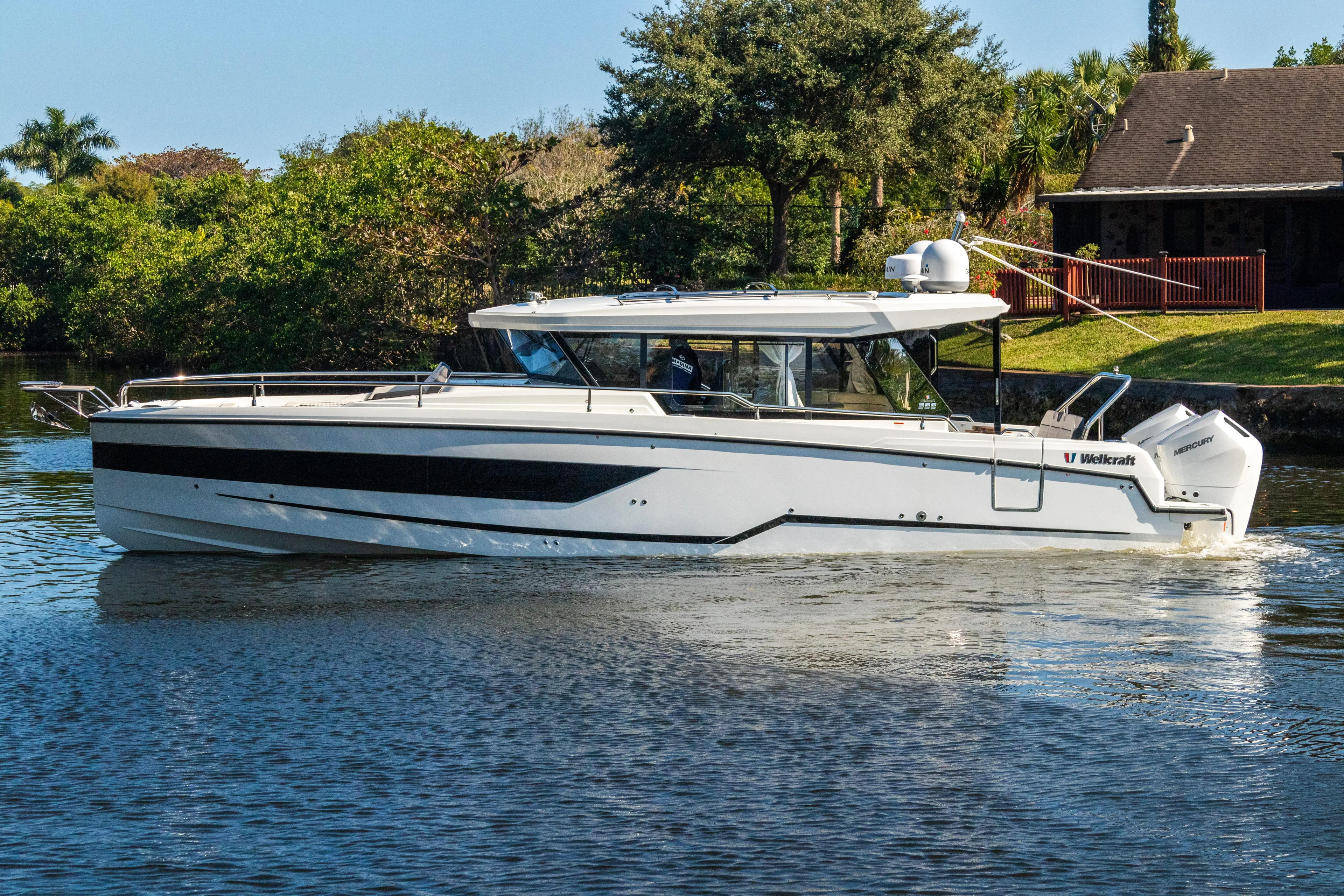  Yacht Photos Pics 2025 Wellcraft 355 boat cruising on a serene waterway near lush greenery.