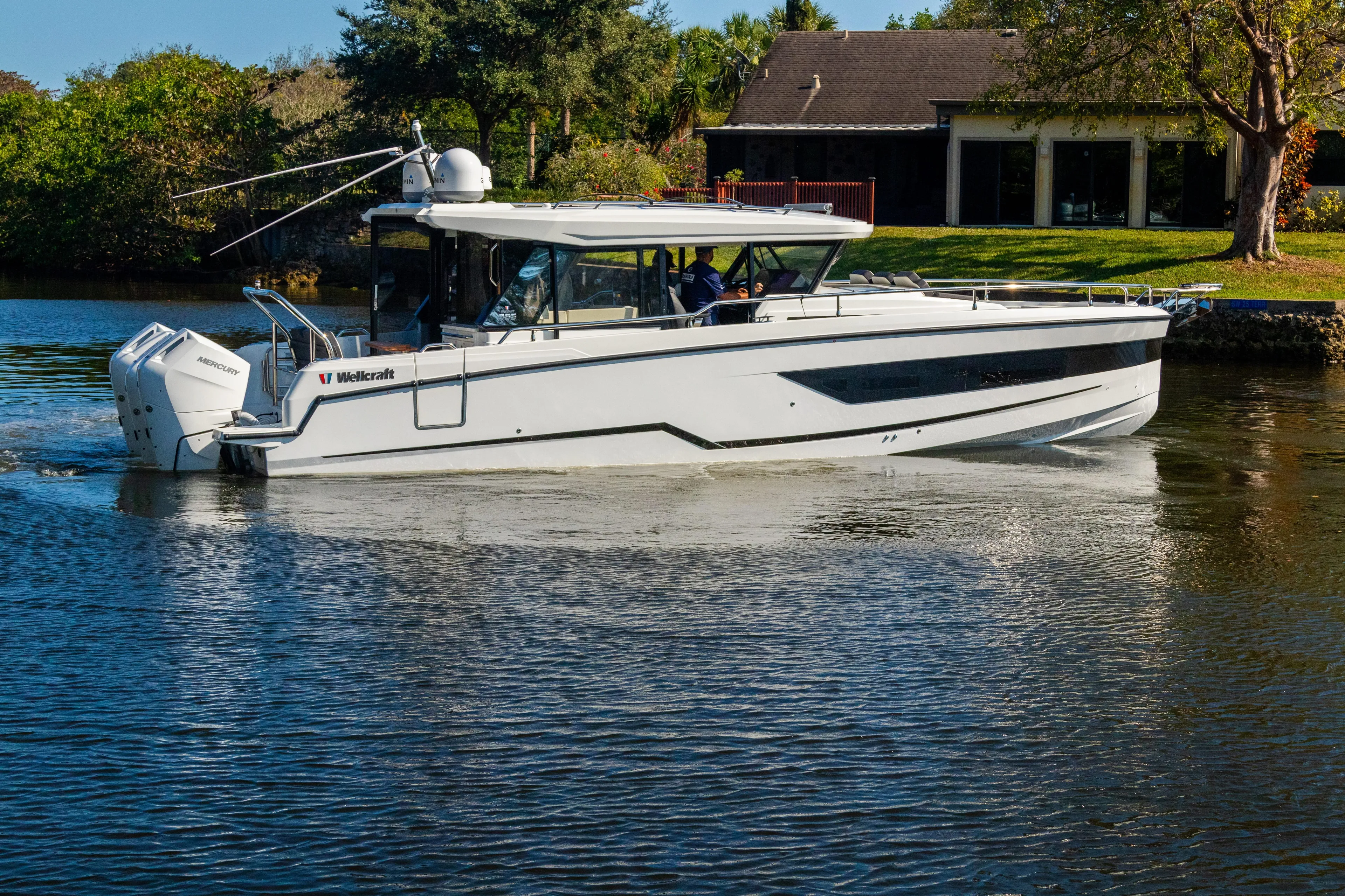  Yacht Photos Pics 2025 Wellcraft 355 boat cruising on a calm river near a house.