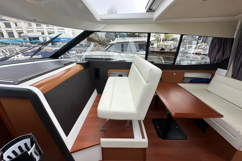  Yacht Photos Pics Interior of 2015 Jeanneau NC11 boat with seating and wooden table in marina setting.