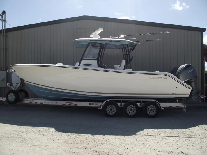  Yacht Photos Pics 2021 Cobia 301 Center Console boat on trailer, parked outside a metal building.