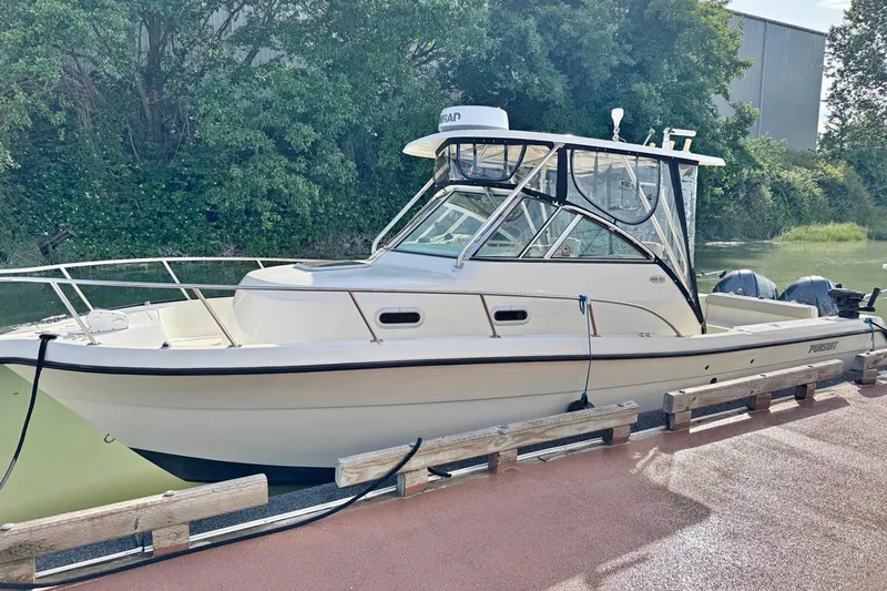  Yacht Photos Pics 2004 Pursuit 2870 Walkaround boat docked by lush greenery.