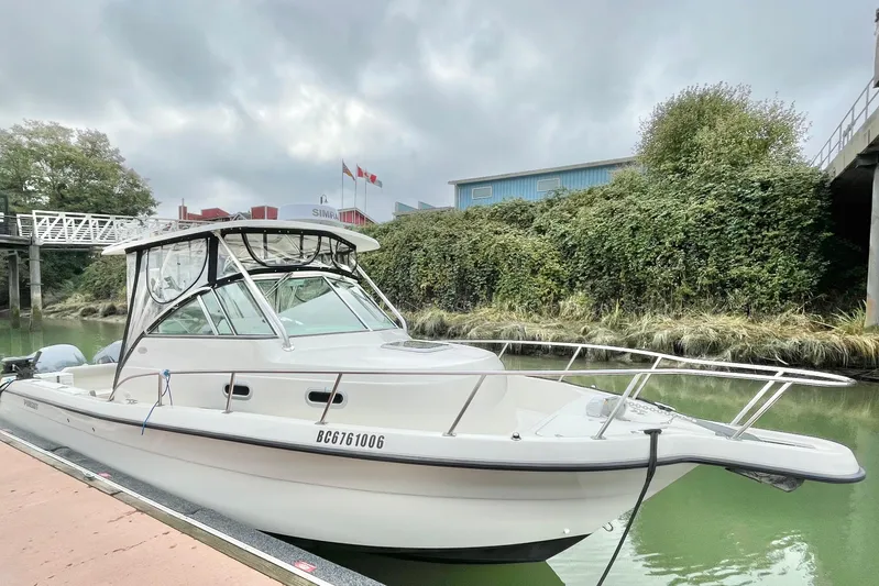  Yacht Photos Pics 2004 Pursuit 2870 Walkaround boat docked by lush greenery under cloudy skies.