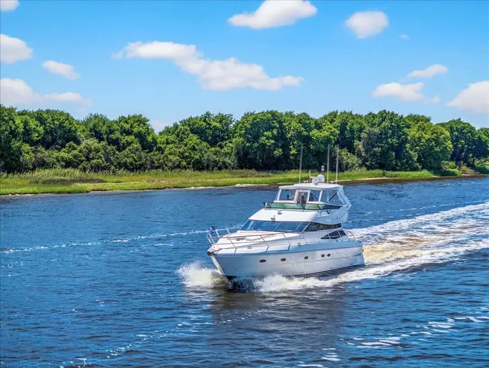  Yacht Photos Pics 2004 Neptunus 56 Flybridge yacht cruising on a scenic river with lush green trees.