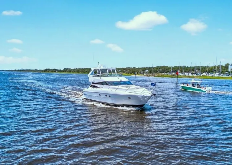 Yacht Photos Pics 2004 Neptunus 56 Flybridge yacht cruising on a sunny day, with a smaller boat nearby.