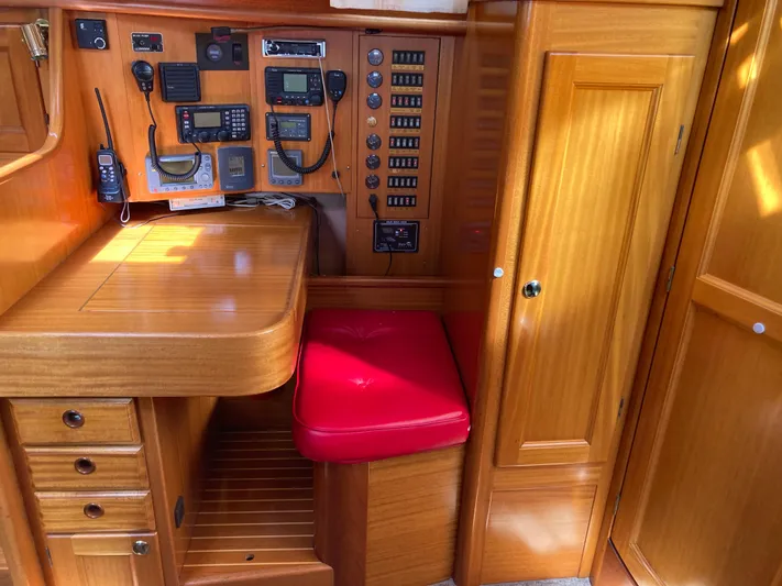 Maloose Yacht Photos Pics Navigation station in a 2001 Malo 43 yacht with wooden cabinetry and red cushioned seat.