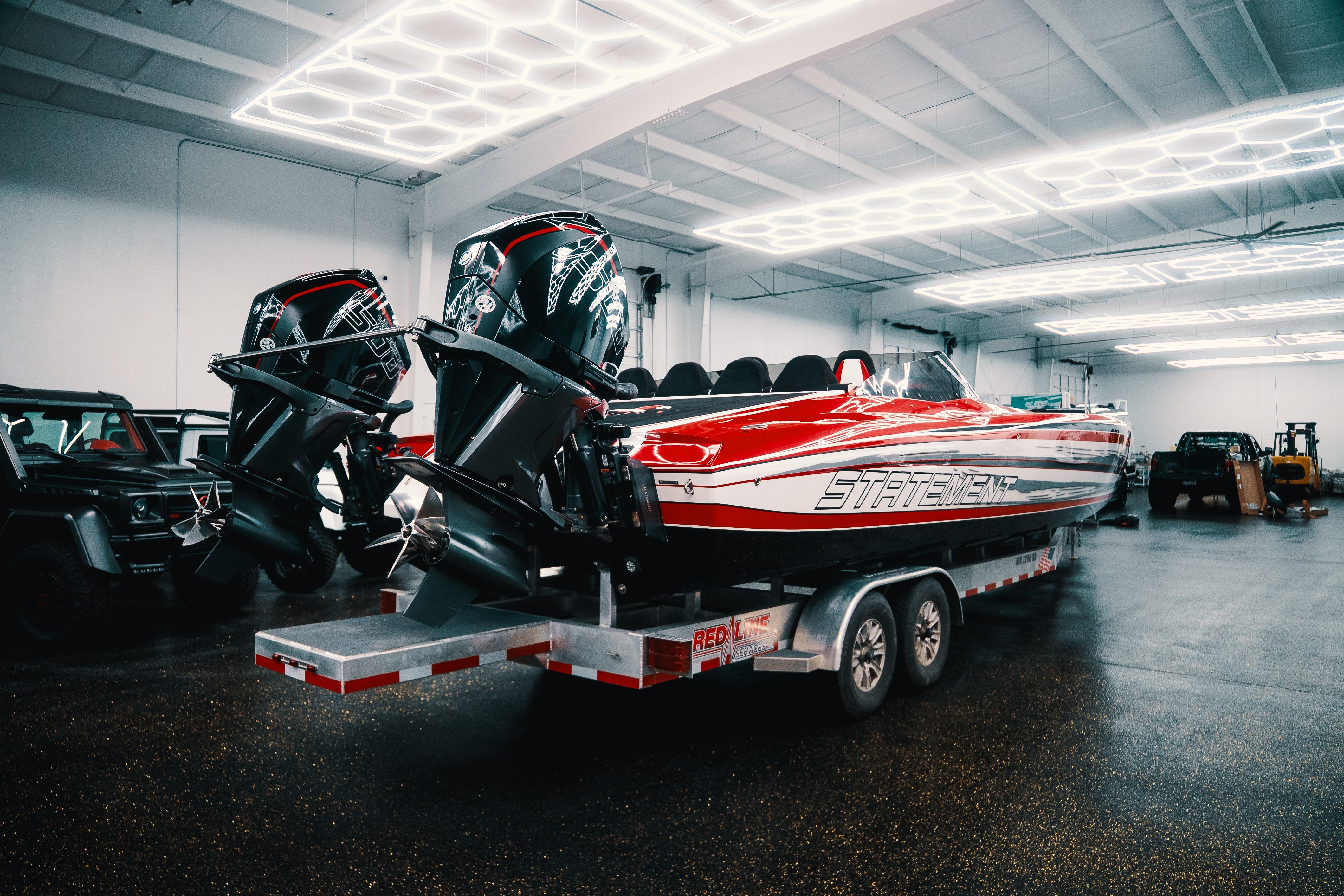 Red and white Statement 360 CAT boat with dual engines on a trailer in a garage.