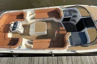 2022 GS 27 boat with wooden deck, spacious seating, and a flag, docked by the water.