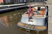 Modern GS 27 boat, 2022 model, docked with a flag, featuring orange seating and a canopy.