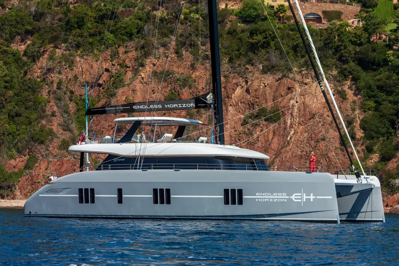 Endless Horizon II Yacht Photos Pics 2022 Sunreef 80 Sail yacht on calm water, with scenic rocky backdrop.