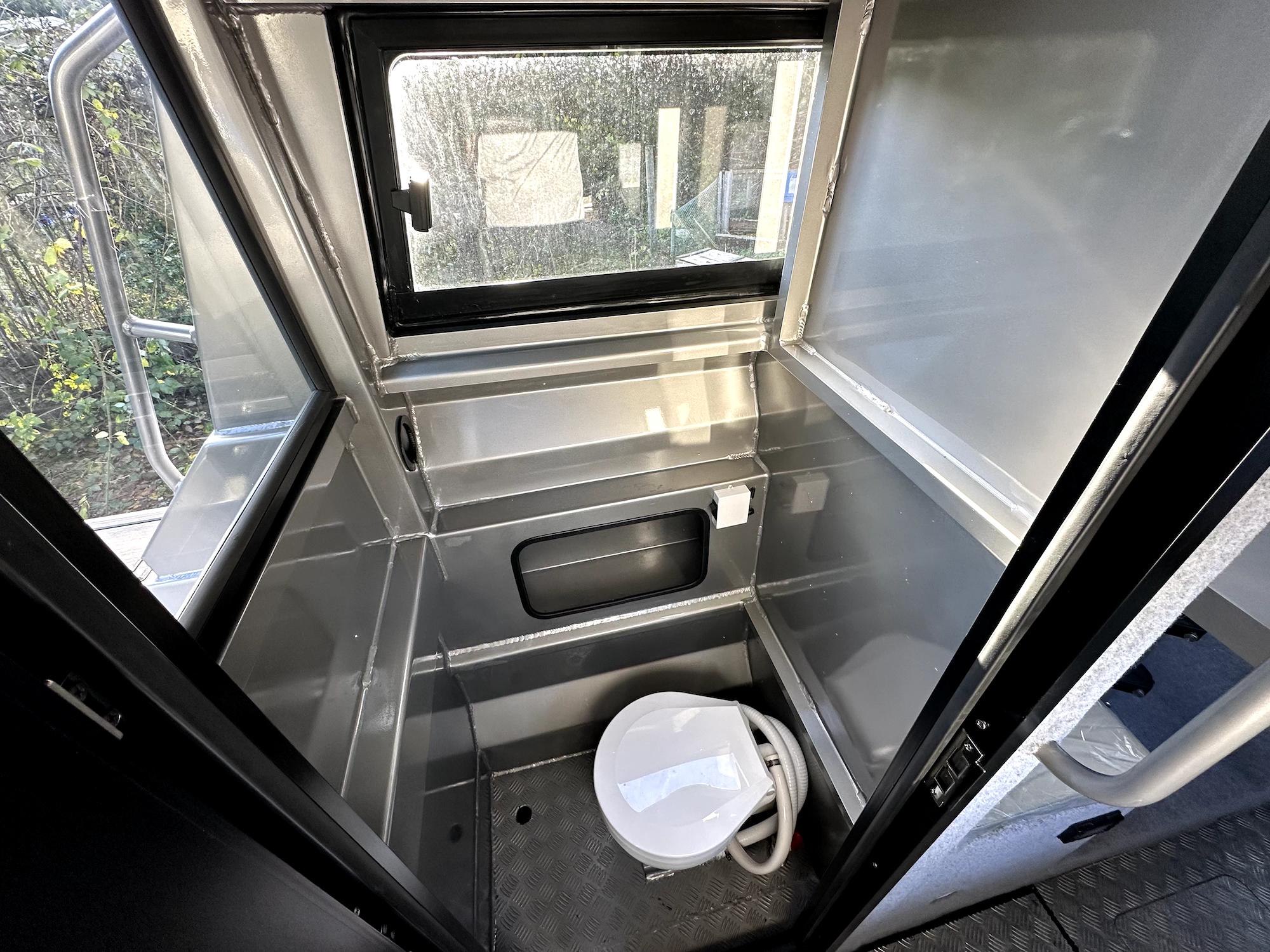 Compact marine bathroom in 2023 Custom Ocean King boat, featuring a toilet and window.