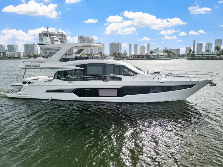 Live More Yacht Photos Pics 2021 Galeon 680 Fly yacht cruising on a sunny day with city skyline backdrop.