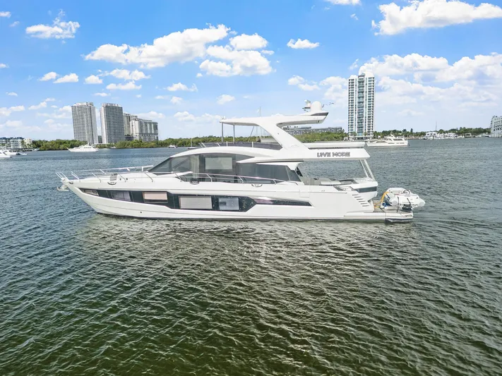 Live More Yacht Photos Pics 2021 Galeon 680 Fly yacht cruising on a sunny day with city skyline backdrop.