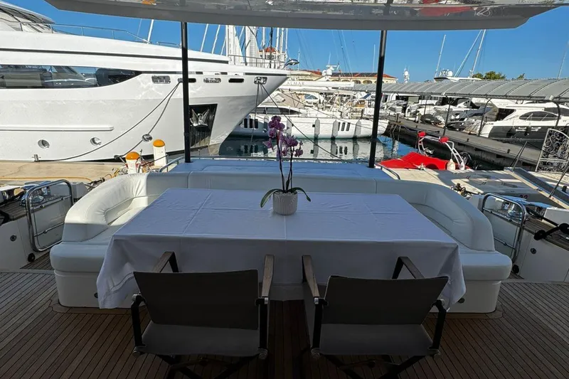  Yacht Photos Pics Luxury yacht deck with dining area, featuring a white tablecloth and potted orchid, docked in marina.