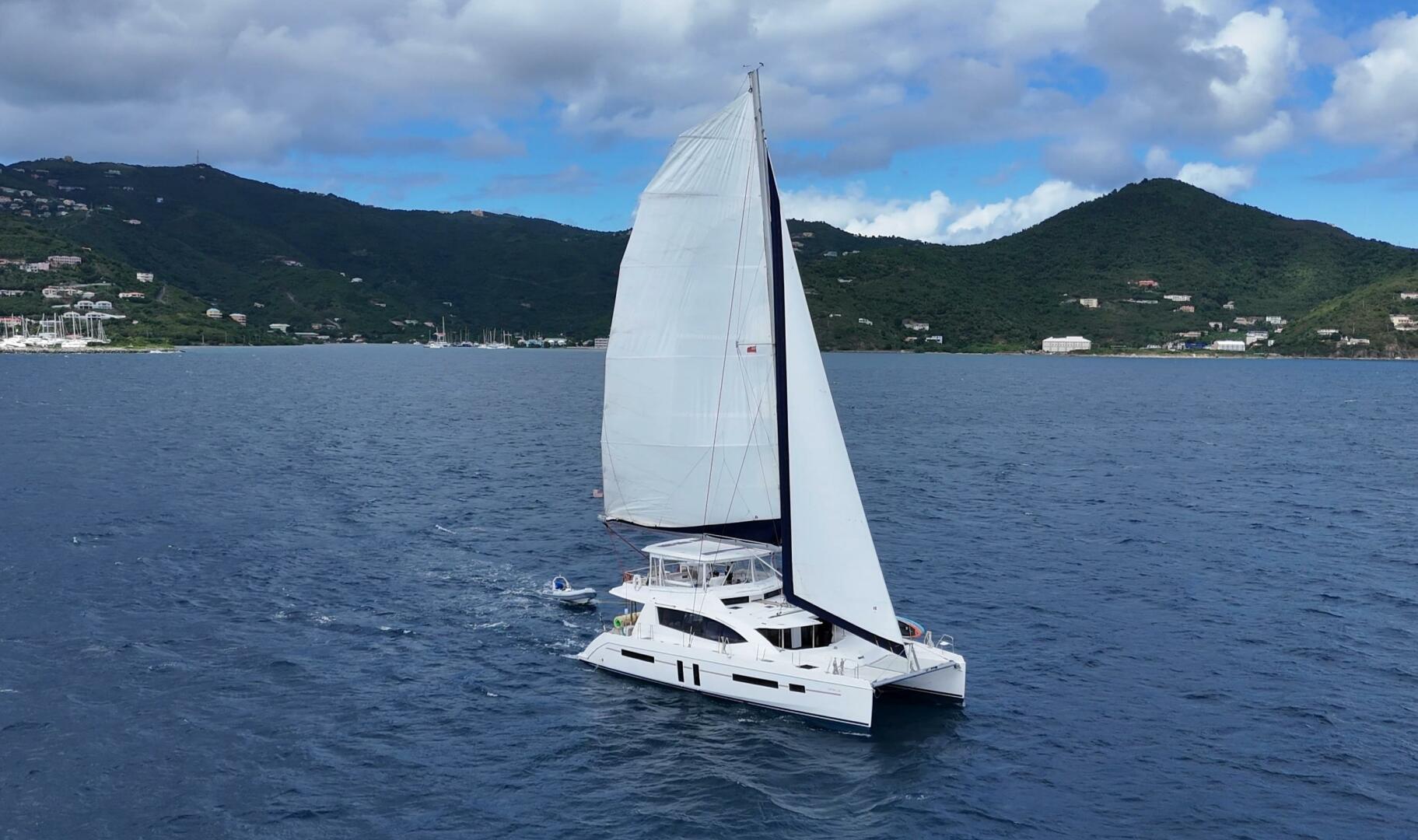 Sailing catamaran Leopard 58 cruising on blue ocean with lush green hills in the background.