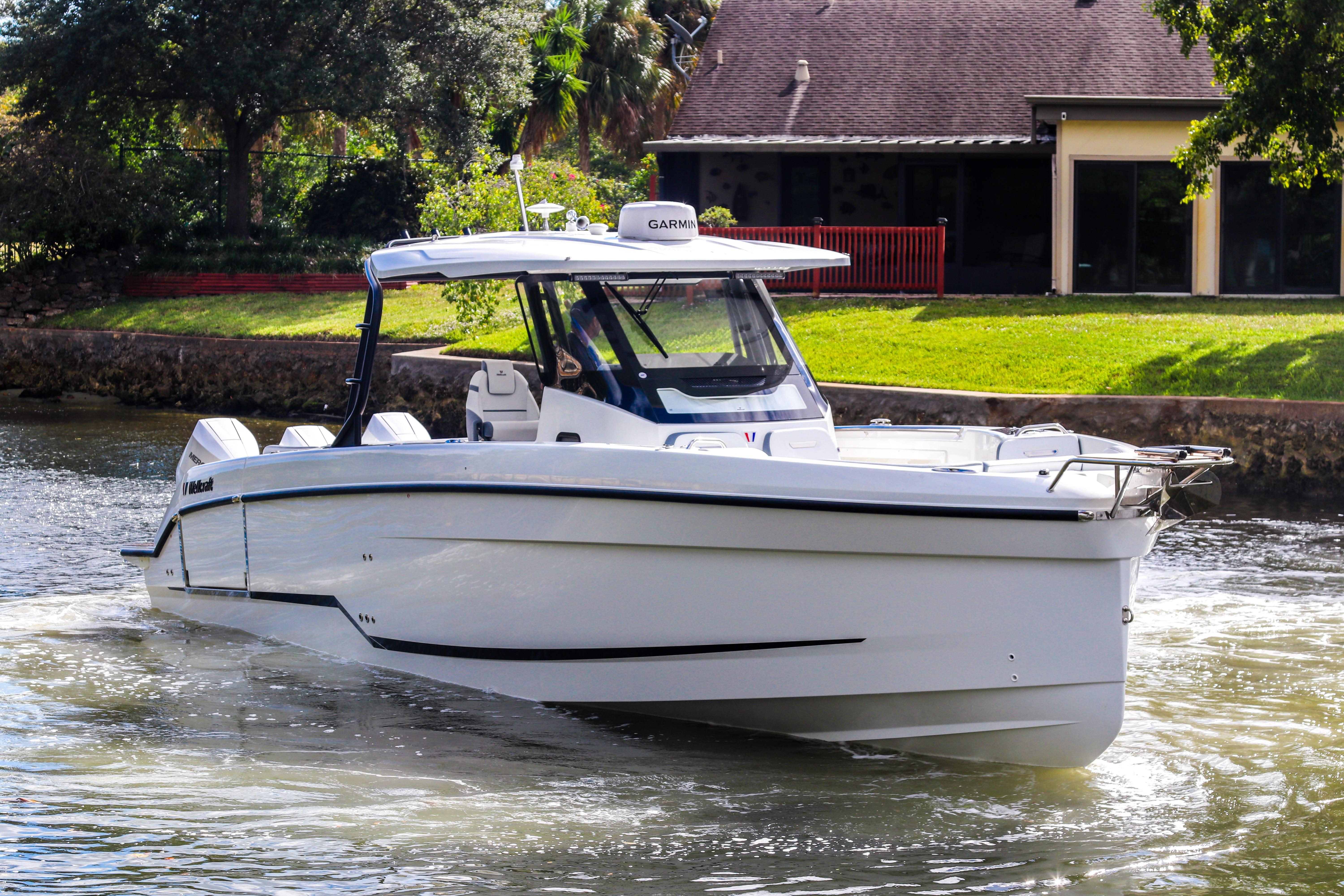 2026 Wellcraft 38 T-Top boat cruising on a sunny day near a waterfront home.