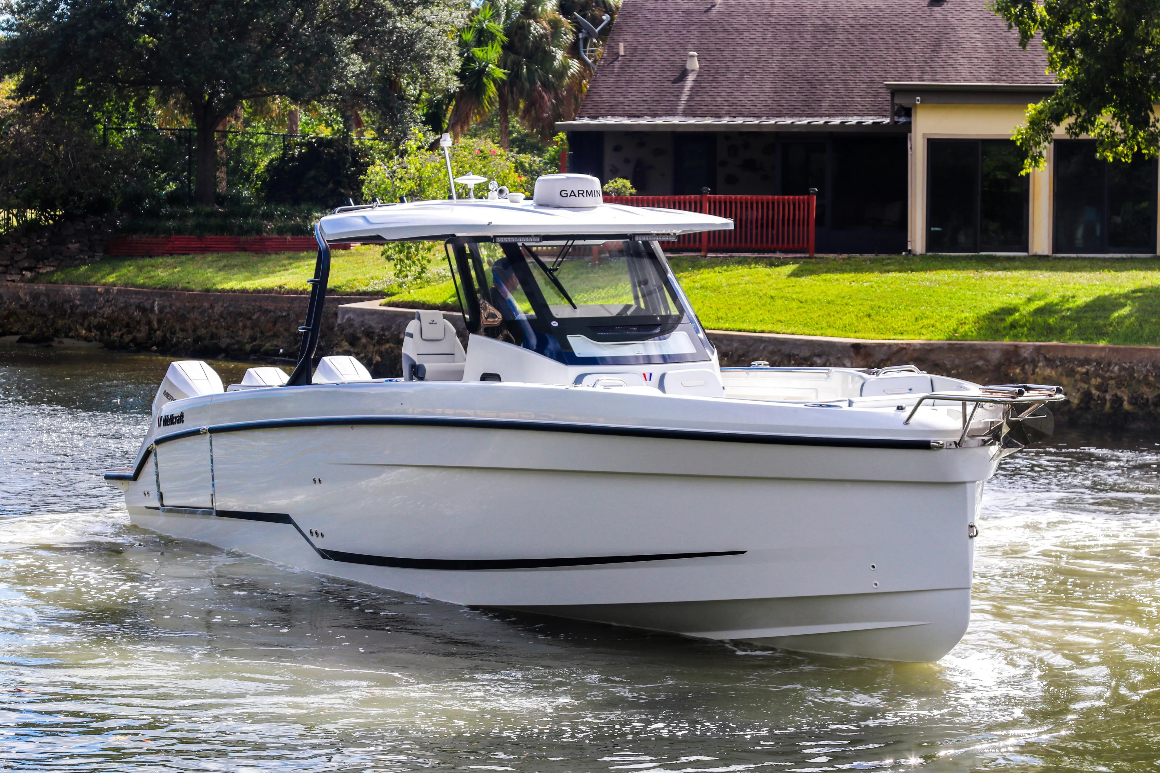 2026 Wellcraft 38 T-Top boat cruising on a sunny day near a waterfront home.