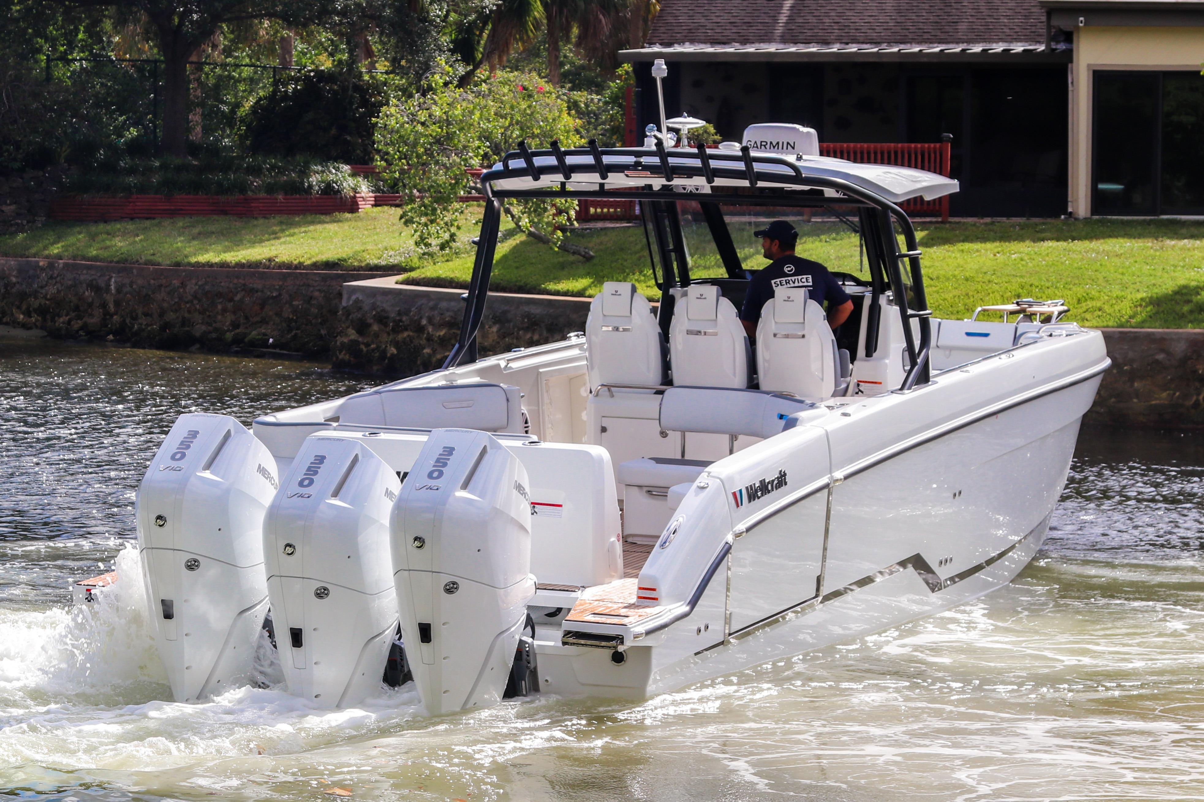 2026 Wellcraft 38 T-Top boat with triple outboard engines cruising on a calm waterway.