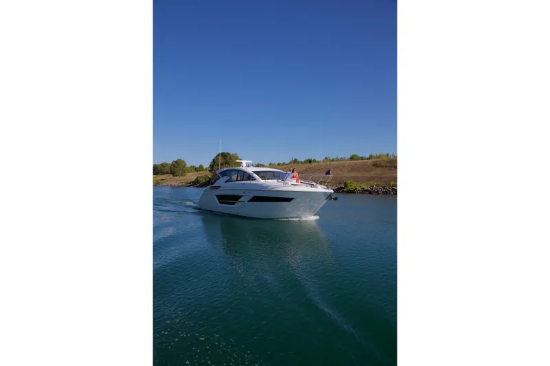  Yacht Photos Pics 2026 Cruisers Yachts 46 Cantius cruising on a serene waterway under a clear blue sky.