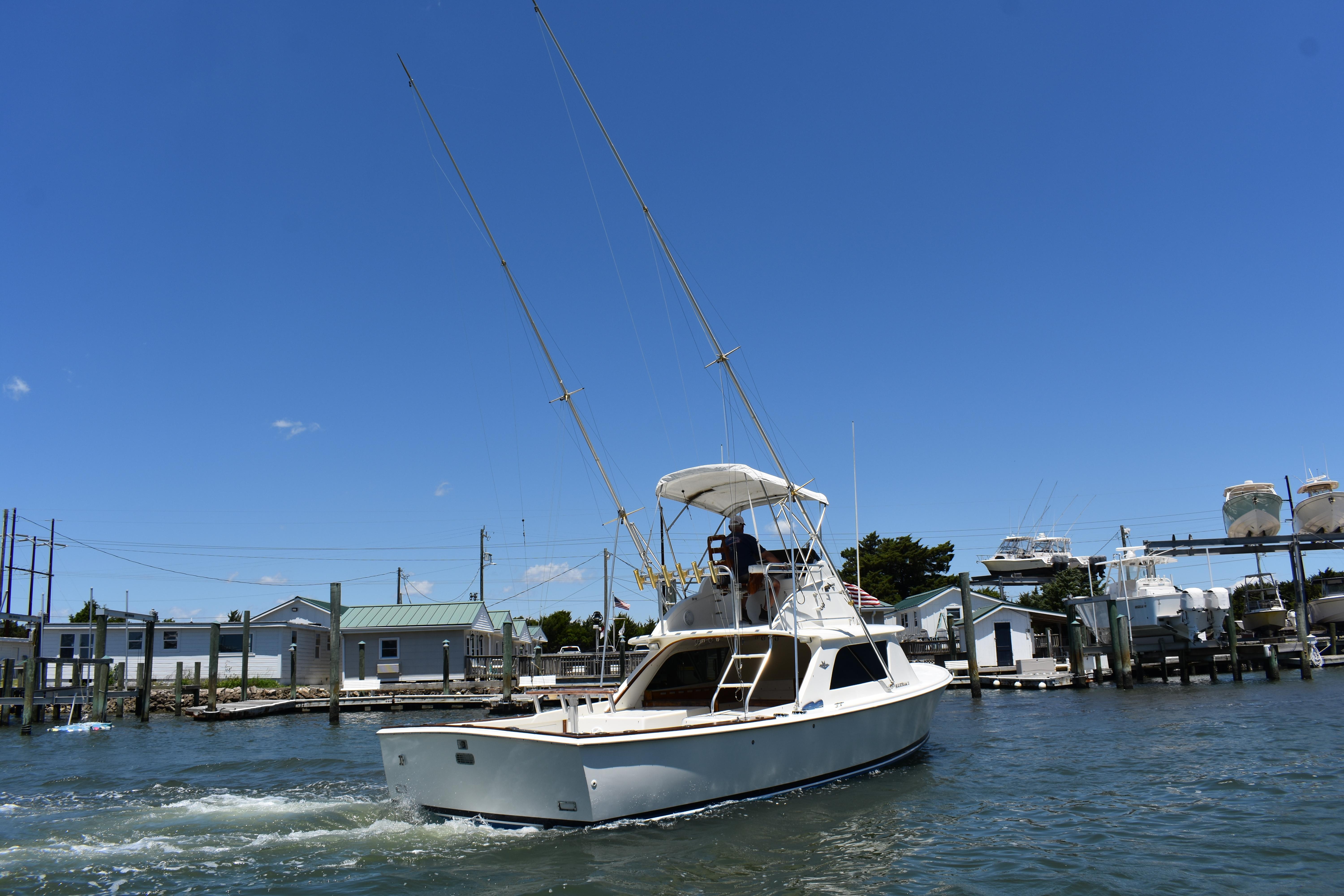 1965 Bertram 31 boat cruising in a marina under a clear blue sky.