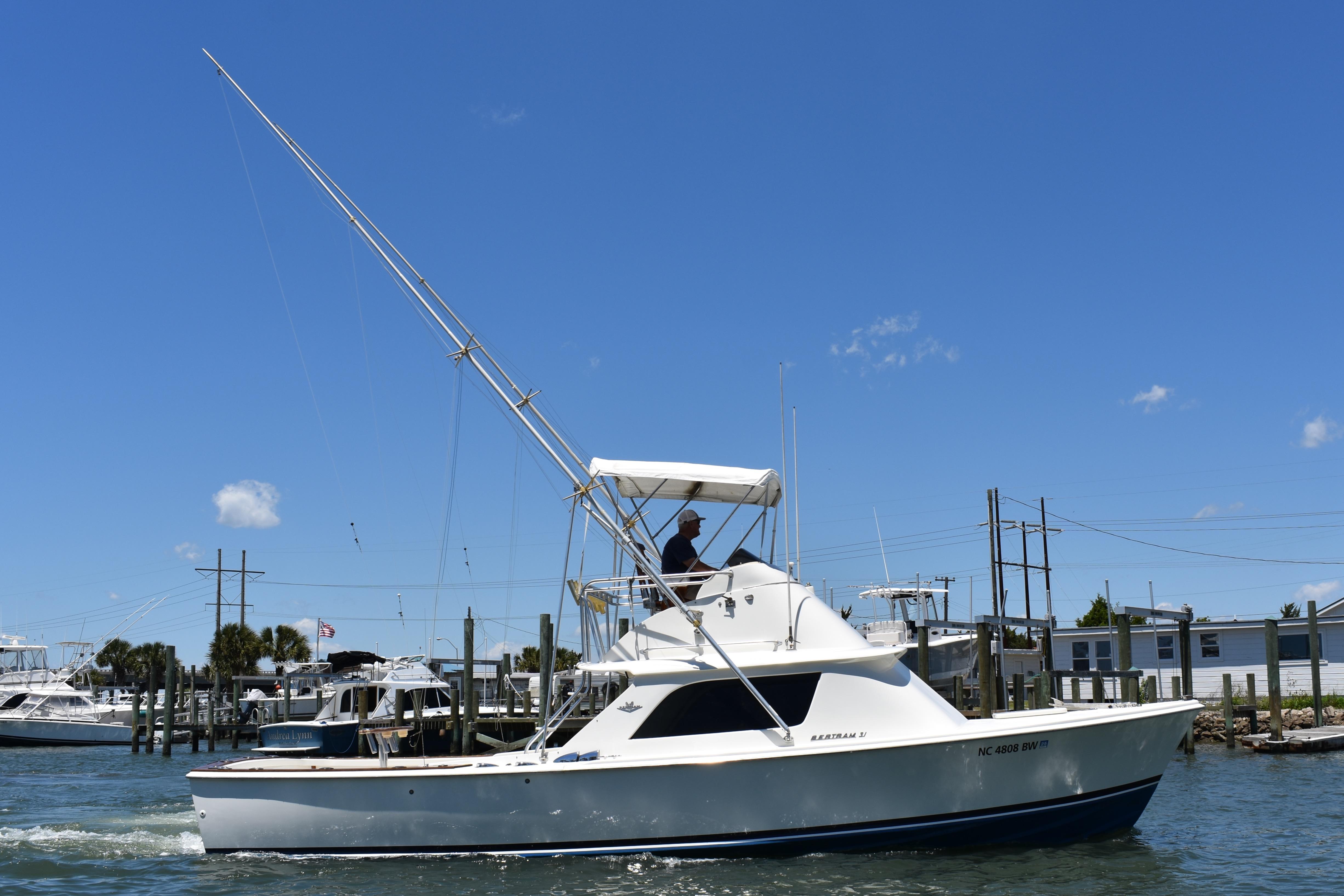 1965 Bertram 31 boat cruising in a marina under a clear blue sky.