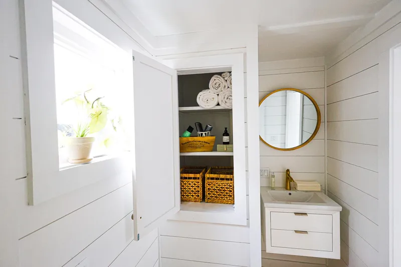  Yacht Photos Pics Modern bathroom on Hank's 40 Houseboat, featuring white shiplap walls, round mirror, and storage shelves.