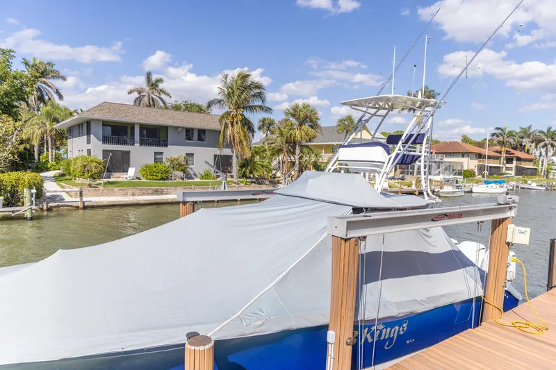  Yacht Photos Pics 2023 Edgewater 370CC boat docked, covered, with waterfront homes and palm trees in the background.