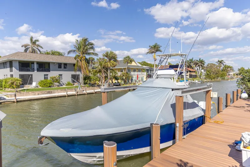  Yacht Photos Pics 2023 Edgewater 370CC boat docked, covered, with palm trees and waterfront homes in the background.