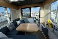 Interior of 2023 Nimbus C11 boat with modern seating and wooden table, overlooking marina.