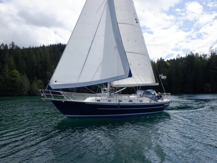 Tapawingo Yacht Photos Pics Sailing yacht Pacific Seacraft 40, 1998 model, gliding on a serene lake with forested backdrop.