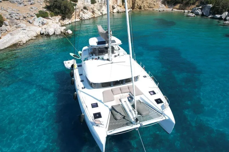  Yacht Photos Pics 2022 Lagoon 50 catamaran anchored in clear turquoise waters near rocky shoreline.